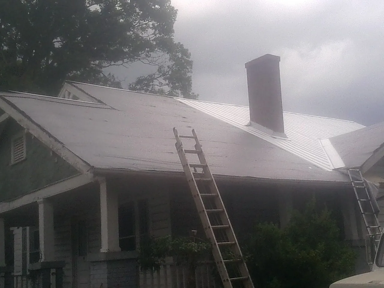 Ladders against a metal roof on an older home with a brick chimney in Townsend