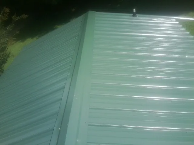 New green metal panels meeting at the ridge of a roof — Flat Roof Repair work by our crew in Townsend